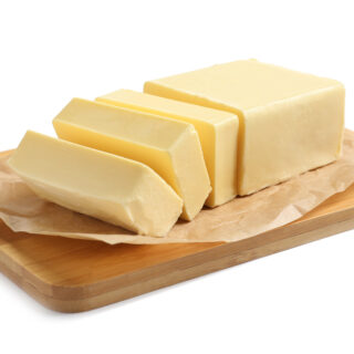 Butter supplies from Middledale for food manufacturing. Wooden board with cut block of butter on white background.