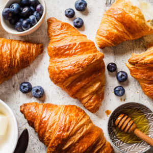 Fresh croissants with blueberries and honey, gray background. Pastries produced using butter suppliers Middledale for product manufacturers in the UK.