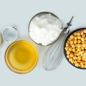 Chickpea aquafaba. Egg replacement. Vegan cooking concept. Whipped chickpeas liquid in glass bowl. chickpea in a ceramic plate. whisk. gray isolated background. Vegan egg replacement ingredient.